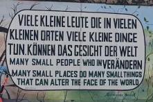 Graffiti auf Mauer mit Spruch: Viele kleine Leute die in vielen kleinen Orten viele kleine Dinge tun können das Gesicht dere Welt verändern - Deutsch und Englisch in großen Lettern