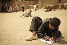 Ein junge schreibt auf einem Blatt Papier, das auf dem staubigen Boden liegt.