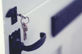Ein Schlüssel steckt in einem Türschloss, darunter eine schwarze Türklinke