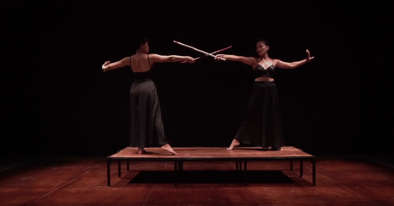 Giant Strey Two women fencing with sticks on a small stage