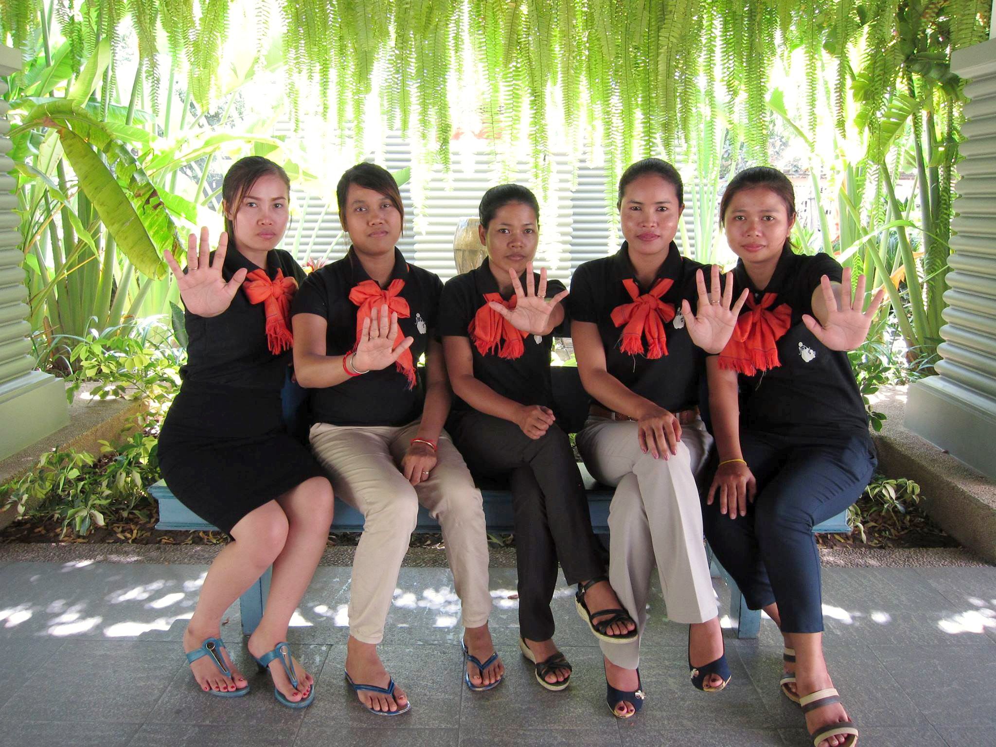 Five women in black dresses are sitting on a bench and showing their show their outstretched hands