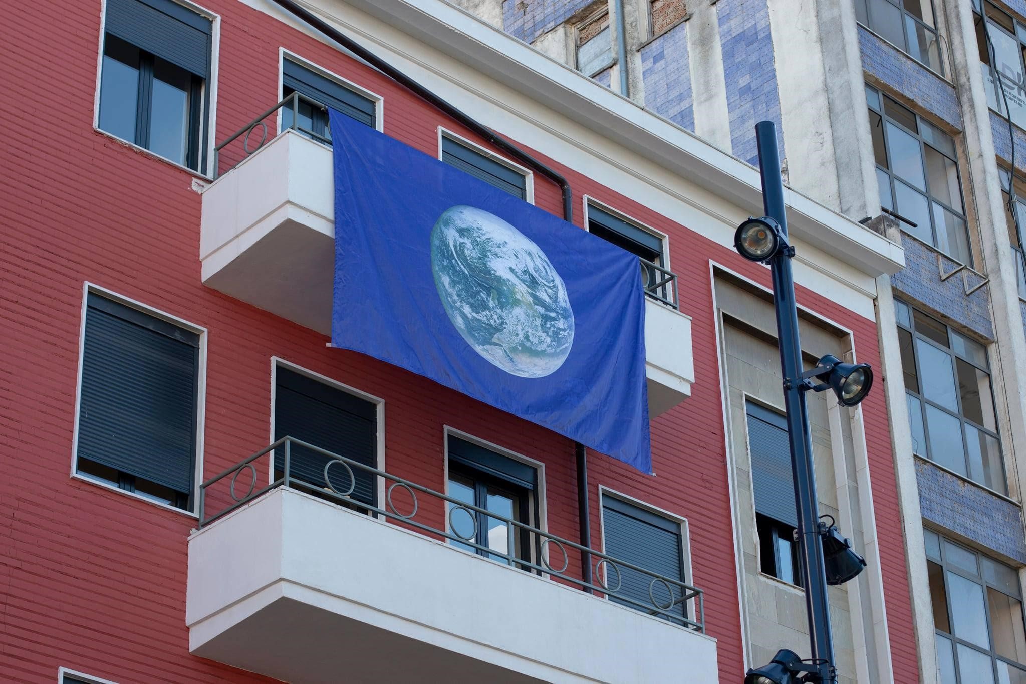 Büro der Heinrich-Böll-Stiftung in Tirana Büro der Heinrich-Böll-Stiftung in Tirana - rotes, mehrstöckiges Gebäude mit am Balkon hängenden blauen Fahne mit Erdkugel