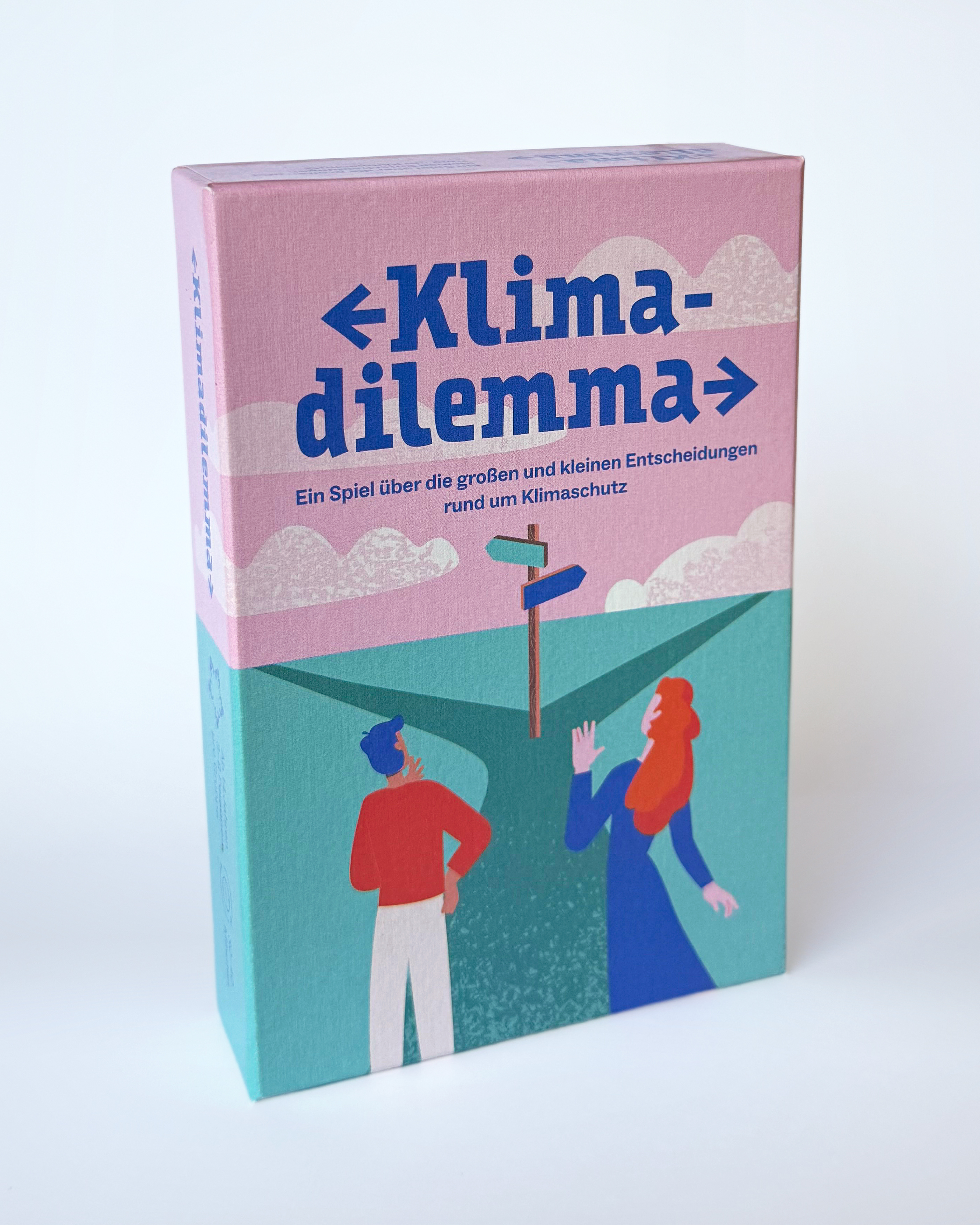 Schachtel mit einer Abbildung von zwei Menschen in Rot und Blau stehen vor einem türkisfarbenen Wegweiser unter rosa Himmel und überlegen, welchen Weg sie für den Klimaschutz wählen sollen.