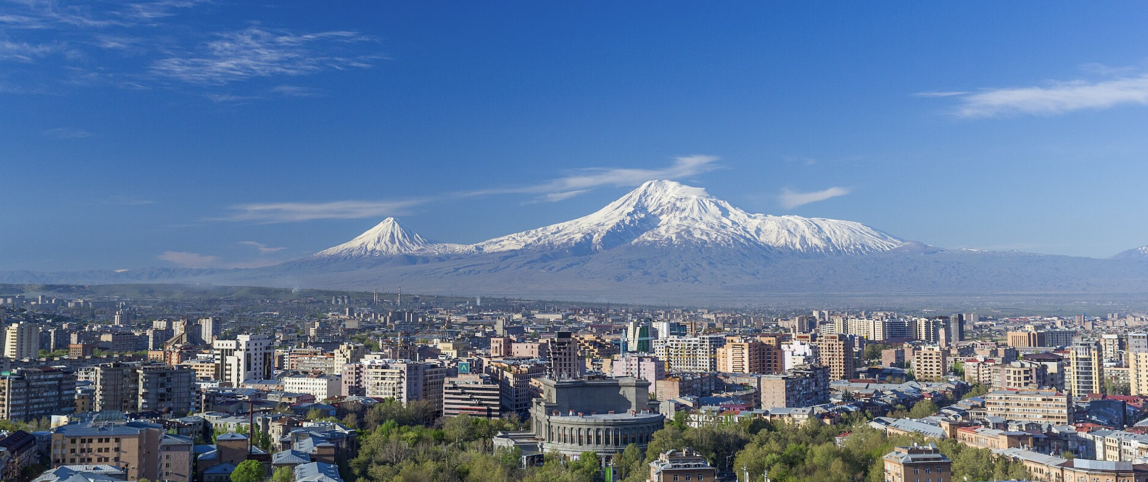 Blick über Jerewan im Frühling mit dem schneebedeckten Berg Ararat im Hintergrund und dem Opernhaus im Vordergrund.