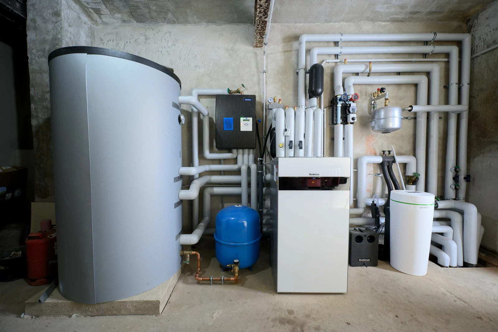 Mehrere Heizungs- und Speichergeräte mit vielen isolierten Rohren an einer Wand in einem Technikraum installiert.