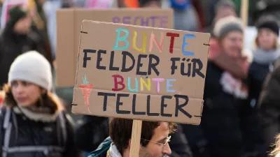 Menschen auf einer Demonstration mit einem Schild, auf dem steht: Bunte Felder für bunte Teller. 