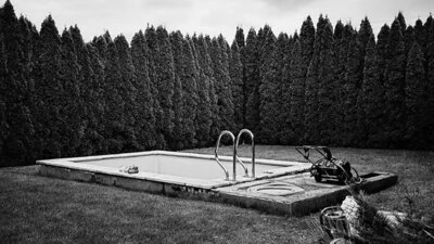 Schwarz-weiß Fotografie von einem Pool umringt von Hecken