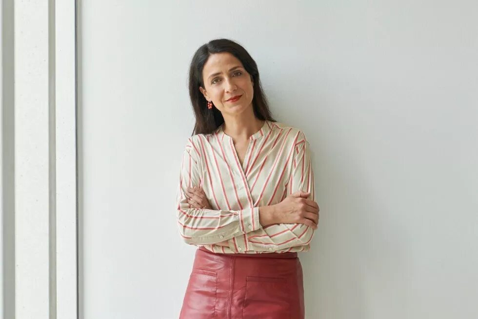 Mirjam Zadoff Porträt von Mirjam Zadoff in rot-weiß gestreifter Bluse, an eine weiße Wand gelehnt.