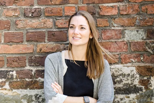 Eliza Diekmann steht mit verschränkten Armen vor einer unverputzten Steinmauer