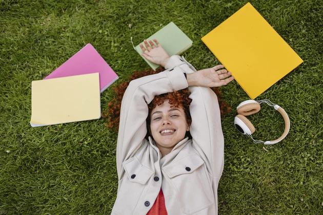 Studentin entspannt im Gras mit Büchern und Kopfhörern im Freien Modell freigegeben, Symbolfoto