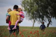 Familienpolitik in Ost- und Westdeutschland: Ein Mann trägt zwei Kinder durch ein Feld