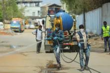 Männer mit Masken reinigen die leeren Straßen in einer Stadt in Indien mit Wasser