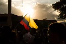 Menschen auf einer Demonstration mit der Fahne Kolumbiens, dahinter ein Sonnenuntergang