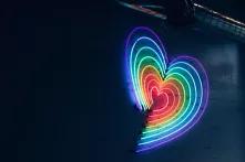 Ein leuchtendes Herz aus LEDs in Regenbogenfarben an einer dunklen Wand