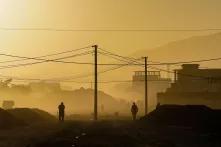 Schwarze Umrisse von zwei Menschen und Strommasten auf einer Straße, dahinter Kabul im gelben Nebel bei Sonnenaufgang