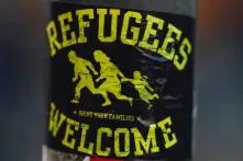 Schwarzer Aufkleber mit der gelben Aufschrift "Refugees Welcome" an einer Straßenmetallsäule
