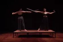 Two women fencing with sticks on a small stage