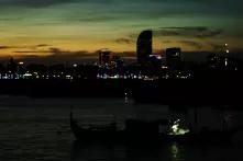 A fisherman is workin on a small boat, in the background is the skyline Phnom Penh