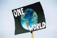 Ein Plakat mit dem Schriftzug "One World" wird in die Höhe gehalten.