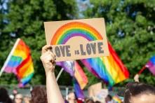 Frauen, die ein Plakatzeichen halten Love ist Liebe mit Regenbogen Symbol der LGBT-Gemeinschaft. Menschenmenge mit Flaggen im Hintergrund. Pride Parade, Gleichstellungsmarsch zur Unterstützung und Feier der LGBT+, LGBTQ Gay lesbische Gleichheit.