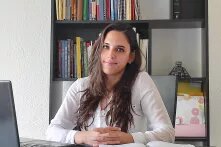 Porträt Diana González Pino. Sie sitzt vor einem Bücherregal