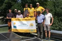 Menschen stehen vor Solarpanelen und halten ein Transparent von SoLocal Energy e.V. in der Hand