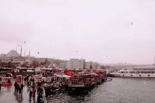 Blick auf den Hafen von Istanbul, an einem Schiff wehen viele türkische Flaggen, darüber ein grauer, regnerischer Himmel