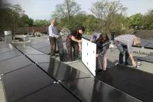 Vier Personen installieren ein Solaranlagenmodul auf einem Flachdach