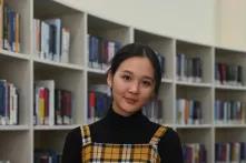 Adiya Akhmer steht in einer Bibliothek und lächelt