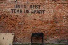 Eine Backsteinwand auf der in schwarzen Buchstaben steht: "Until Debt Tear us Apart"