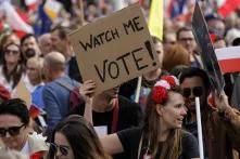 Auf einer Demonstration, auf der polnische Nationalflaggen und EU-Flaggen geschwenkt werden, hält eine Frau ein Pappschild hoch, auf dem steht "Watch me vote"