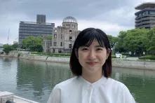 Shizuka Kuramitsu steht vor einem Fluss in der Stadt und lächelt