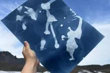Eine Hand ragt in den Himmel und hält ein Foto von schmelzendem Gletscher hoch