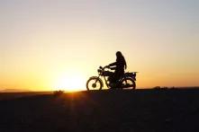Zu sehen ist die Silhouette eines Menschen auf einem alten Motorrad, dahinter die untergehende Sonne