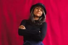 Portrait of Sofia Castillo. She is standing in front of a red background and has her arms crossed.