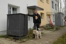 Tobias Zeller steht mit dem Familienhund vor seinem Einfamilienhaus und stützt sich an der Luft-Wasser-Wärmepumpe ab.