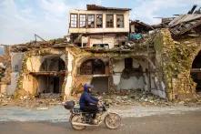 Mopedfahrer fährt an vom Erdbeben zerstörten Haus vorbei