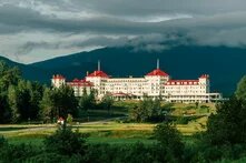 A white building with a red roof with mountains in the background