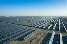 Foto: Großflächige Solarpark-Anlage mit unzähligen Reihen von Solarpaneelen auf einer weitläufigen, trockenen Ebene unter klarem Himmel.