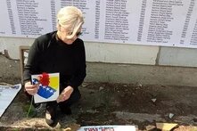 Halida Uzunović kniet vor einem Plakat mit dem Bild und Namen von Enes Uzunovic. Sie hält eine rot-gelbe Blume und das Wappen von Bosnien.