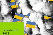 llustration: Ukrainische Flaggen vor einem Hintergrund aus grauen und weißen Rauchwolken. Links unten ein grünes Feld mit der Aufschrift „Jahresbericht 2022“