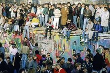 Bunte Menschenmenge steht vor und auf der Berliner Mauer am Brandenburger Tor, am Tag nach dem Mauerfall