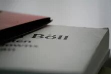 Aufgeschlagenes Buch, teilweise durch ein anderes Buch verdeckt, Name "Böll" deutlich lesbar.