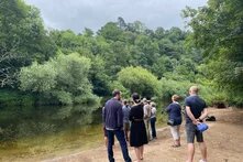 Eine kleine Gruppe Menschen steht am Flussufer des Darts in Devon, UK. 