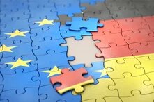 Foto: Ein Puzzle mit Teilen der Europaflagge und der deutschen Flagge, die fast zusammenpassen. Ein blaues Puzzleteil liegt daneben.