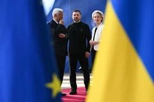 Foto: Drei Personen stehen auf einem roten Teppich, umgeben von EU- und Ukraine-Fahnen. Links António Costa, Präsident des Europäischen Rates, in der Mitte der ukrainische Präsident Volodymyr Zelenskyy, rechts EU-Kommissionspräsidentin Ursula von der Leyen.