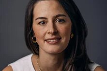 Portraitfotografie von Carolina Mendes. Lächelnde Frau mit weißer Bluse vor grauem Hintergrund.