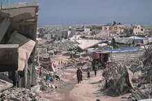 Photo: Destroyed buildings and rubble in Gaza, several people walking along a dusty road.
