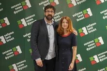 Photo: A bearded man with glasses in a blazer stands next to a woman with shoulder-length red hair and a dark dress in front of a “Zeleno levi front” wall.