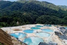 Foto: In einem Tal bei bewaldetem Hügel liegen mehrere runde Wasserbecken mit hellblauer Flüssigkeit und weißen Rohrleitungen.